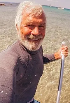 Happy senior active man holding a water paddle while standing in the sea, showcasing cardiovascular health and physical stamina.